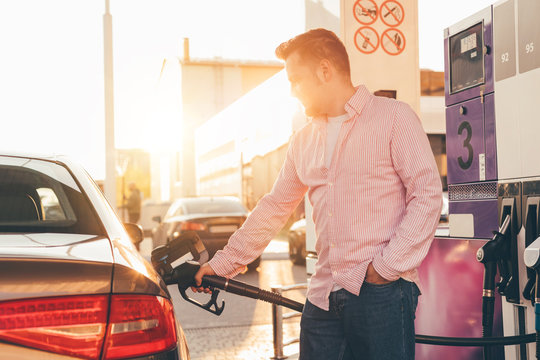 A young man refueling his car tank with petrol at fuel station. Self-service. Sunset lighting