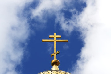 Close-up of the Orthodox golden cross on the roof of the Church against the background of blue sky and clouds