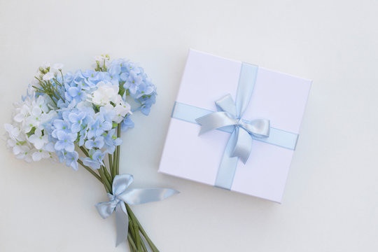 Top view of flower, white gift box with blue ribbon on white background