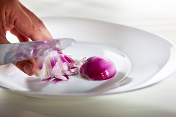 Someone´s hand chopping the purple onion on the white plate