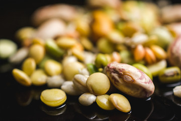 Close up shot of different kind of legumes on a black reflective surface