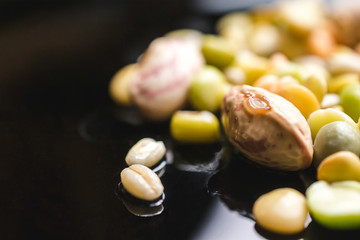 Close up shot of different kind of legumes on a black reflective surface