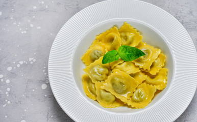 Ravioli with ricotta and spinach in a white plate on a grey stone table. Recipe of Italian pasta, gourmet lunch.  Top view , copy space , food  flat lay