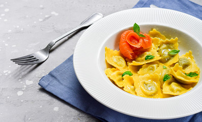 Salmon ravioli traditional Italian food with fresh basil  in a white plate on a grey stone table. Recipe  Italian cuisine, . Top view , copy space , food flat lay