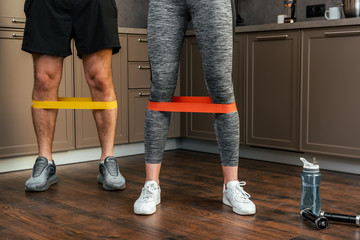 cropped view of couple exercising together with resistance bands on legs at home during quarantine