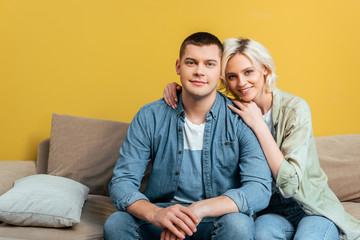 happy young couple hugging on sofa near yellow wall