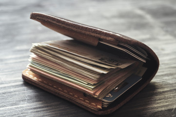 Old leather wallet full of money on wooden background