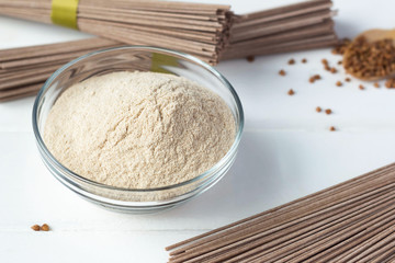 buckwheat flour in a plate, buckwheat is scattered on the table, soba lies nearby