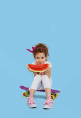 Happy little girl show language and biting a big piece of watermelon, sitting on a skety blue background. Vertical view.