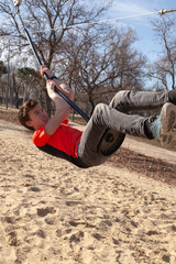 Teenager laughing happily, riding upside down on a bungee swing on the playground. Happiness, freedom, enjoyment, health. Bright summer day.
