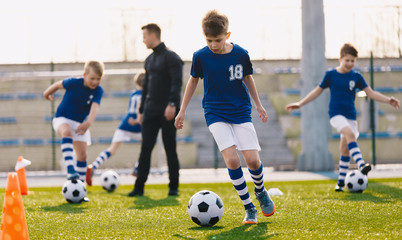 Portrait of school boys training soccer with young coach on football field. Boys running with football balls between colorful soccer markers and cones. Practice sessnion for youth soccer team.