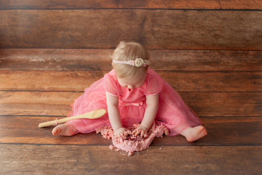 One year old baby celebrates birthday. Photo zone. Cute dress in pink color. Disgruntled little kid. Smash cake. 