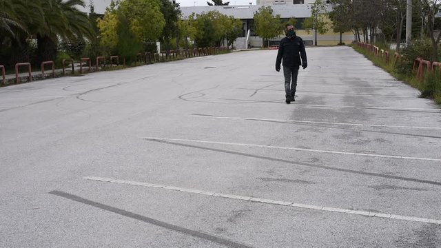 Man wearing his protective mask and gloves walking in an empty parking - mask and gloves during covid 19 pandemic threat