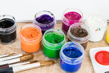 On the table are multi-colored gouache in a jar and brushes for painting. Set for drawing, creativity and hobbies.