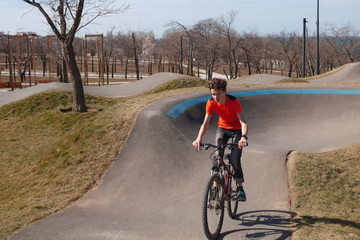 A teenager rides a bicycle on a pump track in a spring park, a guy goes in for sports