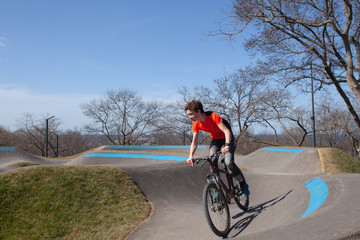 A teenager rides a bicycle on a pump track in a spring park, a guy goes in for sports