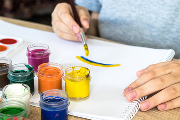 The child draws gouache on a white sheet and jars of paint are on the table. Hobbies and...