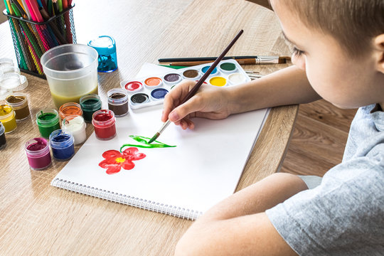 The child draws gouache on a white sheet and jars of paint are on the table. Hobbies and entertainment for children.