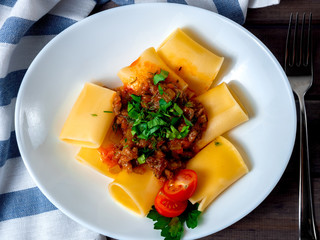 Pacheri pasta with tomato sauce and minced meat on a white plate, top view
