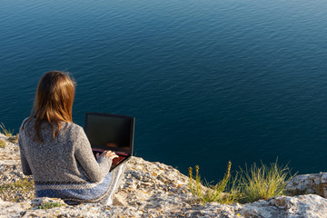A girl is working on a laptop at the top of a mountain. Remote work and training in nature. Sea...