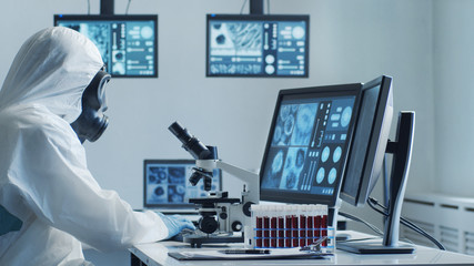 Scientist in protection suit and masks working in research lab using laboratory equipment:...