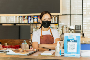 Women cafe owner wearing protective mask stand in counter Covid-19 conceptual.