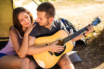 A man plays for a woman on a guitar near a tent at sunset. Honeymoon in the hike