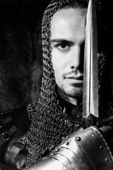 Portrait of handsome knight in suit of armour looking at camera with candles in background