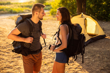 A man and a woman in a hiking trip with backpacks near a tent at sunset. Honeymoon in nature