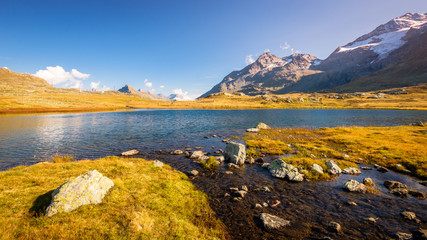 Obraz premium Sun is setting at Lej Pitschen, together with Lej Nair and Lago Bianco one of three lakes at The Bernina Pass. It connects Swiss Engadin valley with Val Poschiavo and ends in the Italian town Tirano
