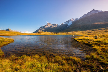 Fototapeta premium Sun is setting at Lej Pitschen, together with Lej Nair and Lago Bianco one of three lakes at The Bernina Pass. It connects Swiss Engadin valley with Val Poschiavo and ends in the Italian town Tirano