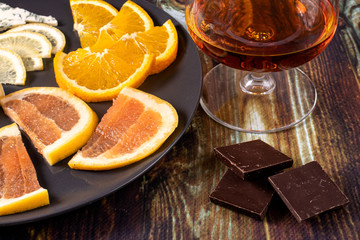 Cognac in a glass and an appetizer for cognac (chocolate, lemon, orange and grapefruit). Appetizer for alcohol, dear spirits.