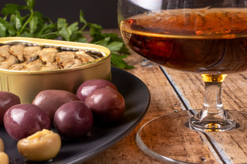 Cognac in a glass and an appetizer for cognac (olives with stones, sprats, pickled champignons). Snack for alcohol.