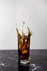 The drink is splashed out of a glass cup, spatter and a splash of beverage. Throwing ice in a glass...