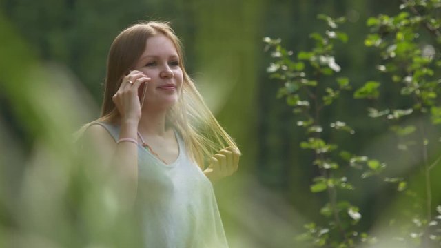 Attractive beautiful girl in summertime outdoors in a good mood communicates on the phone. Green around. Close up
