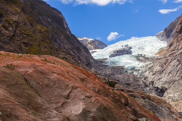Naklejka na ściany i meble Red boulder on a background of a glacier. View of Franz Joseph Glacier in New Zealand