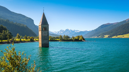 Lake Resia (Reschensee) and Ortler Mountains in Val Venosta (Alto Adige, Italy). It is famous for the tower of a 14th-century church of village Graun that submerged when the lake was deepened in 1950 - obrazy, fototapety, plakaty