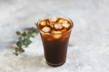 Ice black brew coffee with milk in tall glass with pieces of ice on a grey dark background, close up, natural light, fresh summer drink