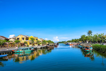 Naklejka na ściany i meble Hoi An ancient town in the sunshine day with blue sky, fishing boats, ancient houses reflect on the river. Hoi An is a popular tourist destination in Quang Nam, Vietnam. Landscape photography.