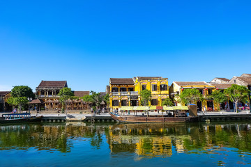Fototapeta na wymiar Hoi An ancient town in the sunshine day with blue sky, fishing boats, ancient houses reflect on the river. Hoi An is a popular tourist destination in Quang Nam, Vietnam. Landscape photography.