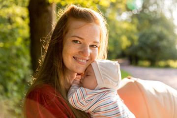 Young mother gently applied to her chest her two-month-old newborn baby in the summer green park....