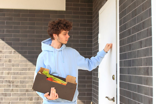 A courier in a protective mask and a glove delivers food to a woman.