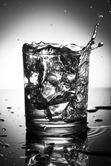 glass of water with splash from falling ice cube, black and white photography .