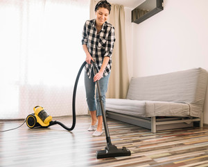 Full shot smiley woman vacuuming. Home clean