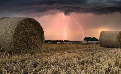 Summer thunderstorm and lightning and looms over harvested hay field with hay bales in the Kempen area, Belgium - Powered by Adobe