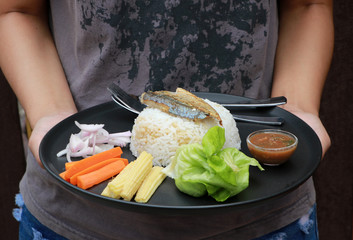 Hand served breakfast in the black round plate. Fried mackerel and Rice with Spicy Shrimp Paste Dip and vegetable, Chinese cabbage, baby corn, carrots and sliced onions.