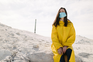 Young woman walking on a phosphate mountain that was made by chemical plant waste. She is wearing yellow protective coat and a mask. Ecology protection awareness