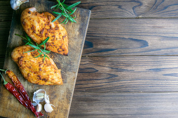 Spicy baked chicken breast with peper, rosemary an garlic on wooden cutting board on wooden table....