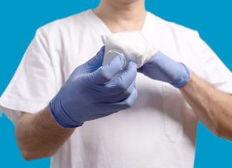 A male doctor surgeon in white uniform puts on blue gloves.