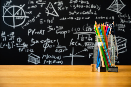 Education background concept. Stationery in glass jar color pencil, compasses tool, scissors, rulers, sharpener On chalkboard with the Mathematical formula background.